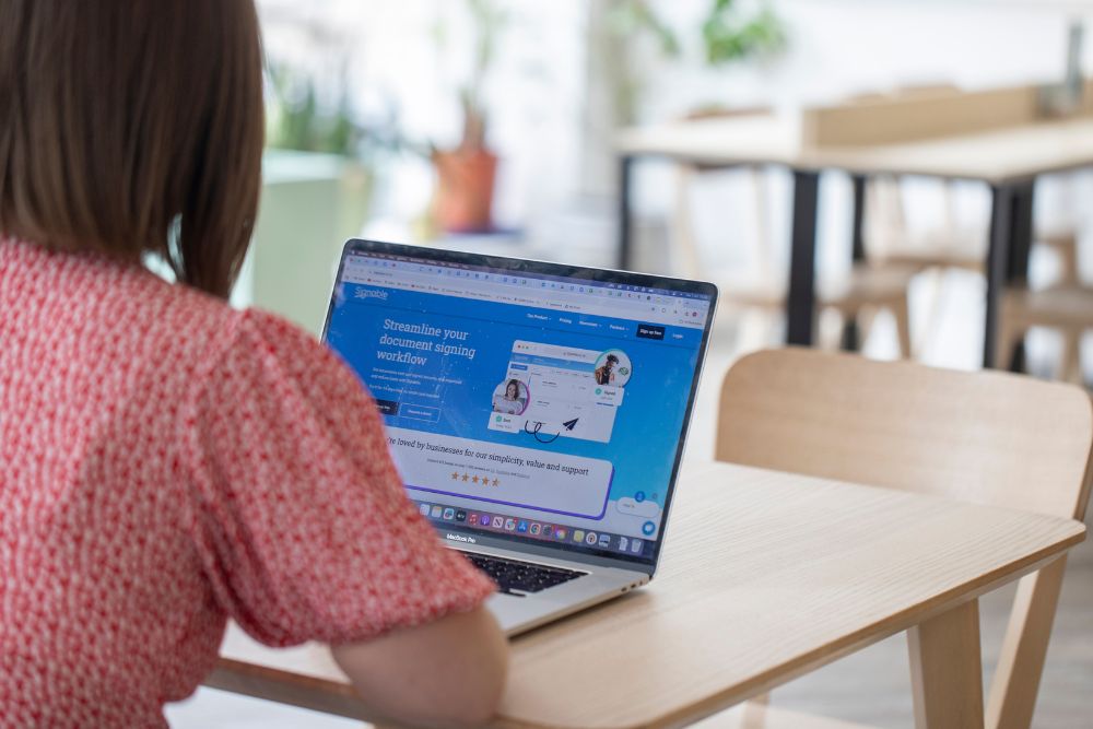 Woman on laptop in coffee shop looking at the Signable website