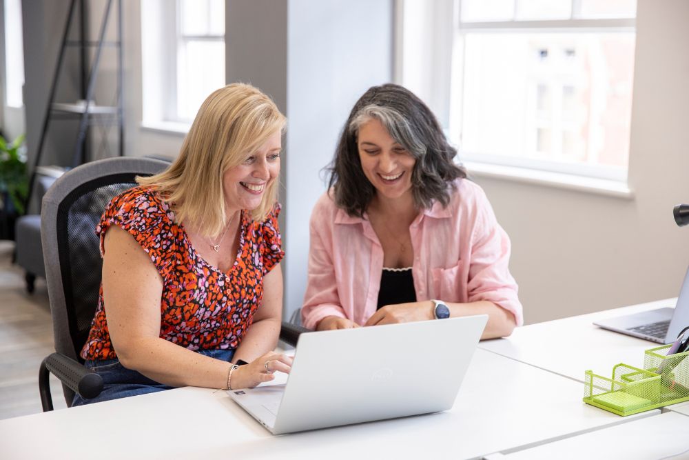 Two women in pink looking at a laptop smiling