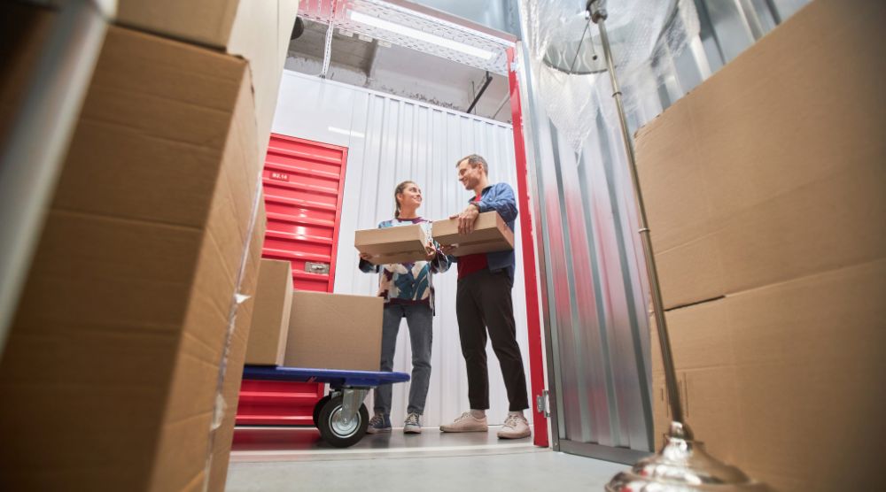 A man and woman putting cardboard boxes into a storage unit